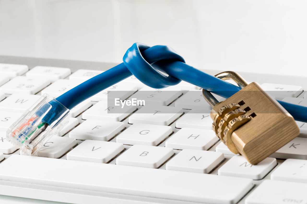 Close-up of padlock and cable on computer keyboard against white background