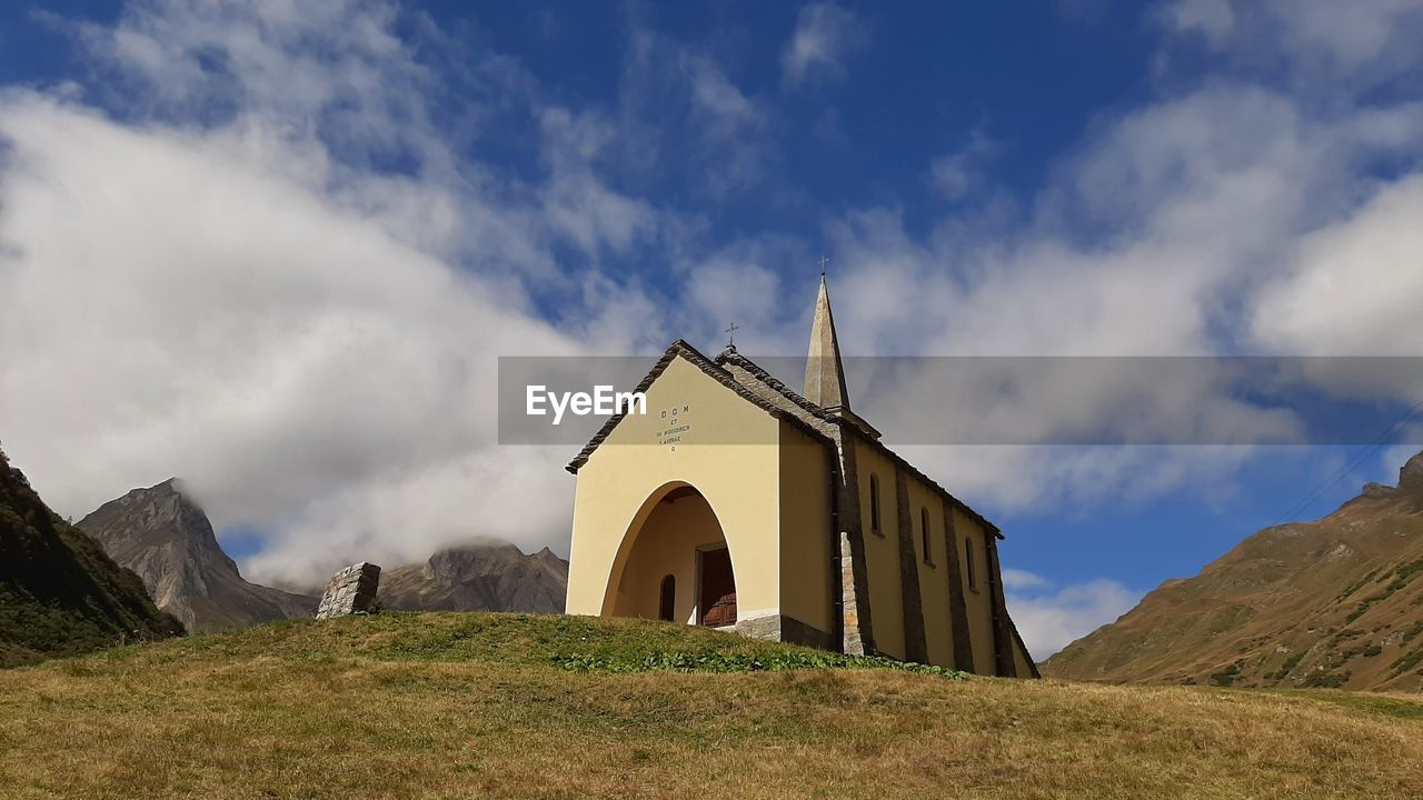sky, cloud, architecture, built structure, hill, nature, religion, rural area, landscape, place of worship, mountain range, building exterior, environment, panoramic, highland, belief, grass, building, land, spirituality, no people, scenics - nature, travel destinations, arch, plant, outdoors, history, beauty in nature, travel, the past, day, catholicism