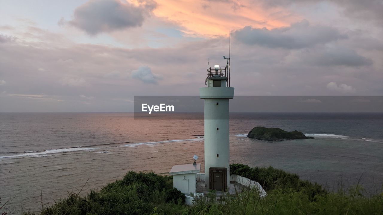 Lighthouse by sea against sky during sunset