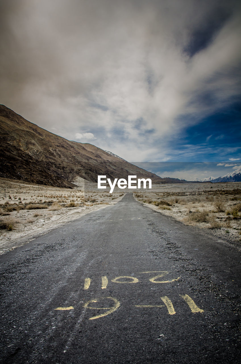 Road leading towards mountain against cloudy sky