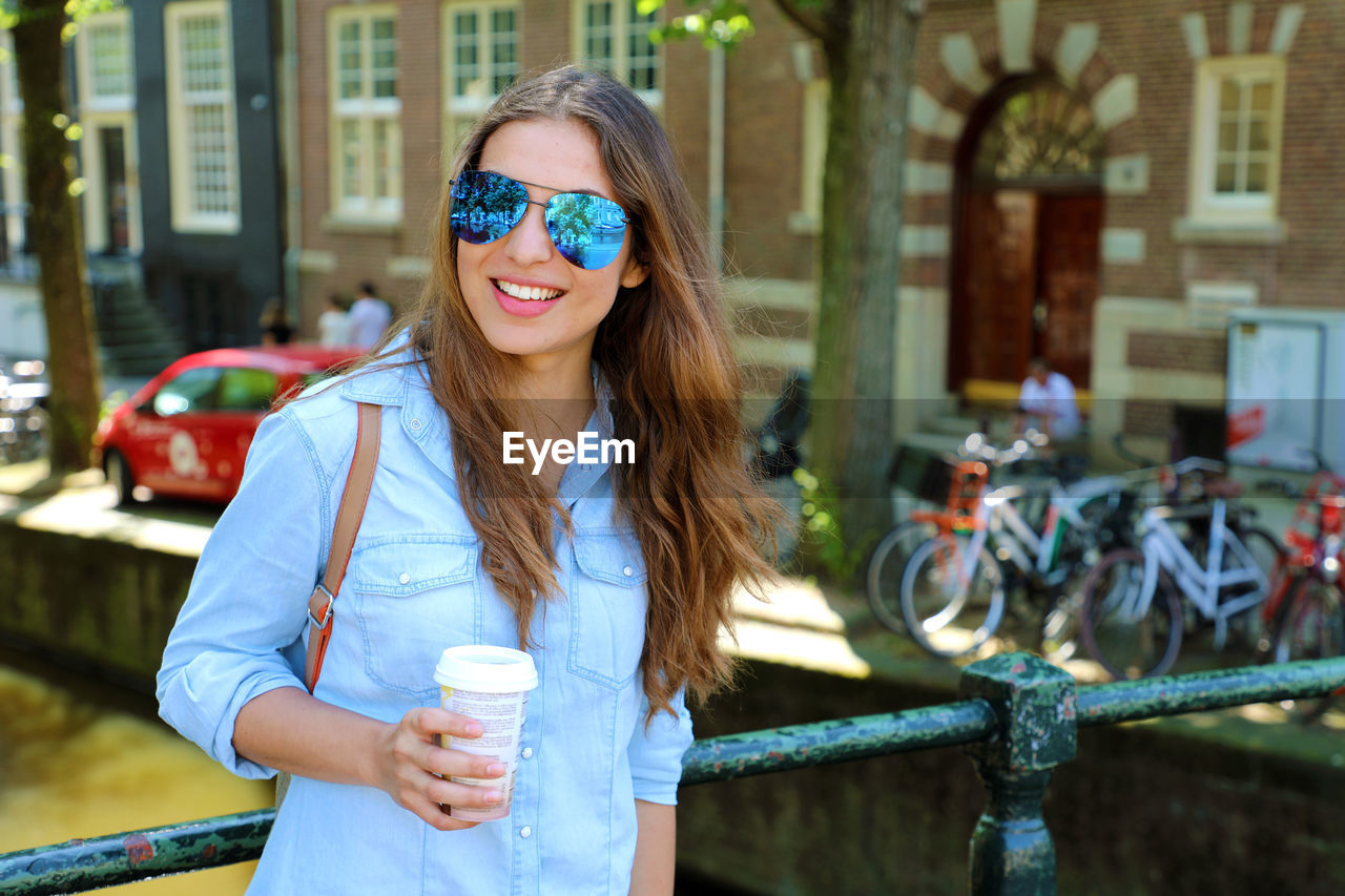 Young woman wearing sunglasses and holding disposable cup of coffee