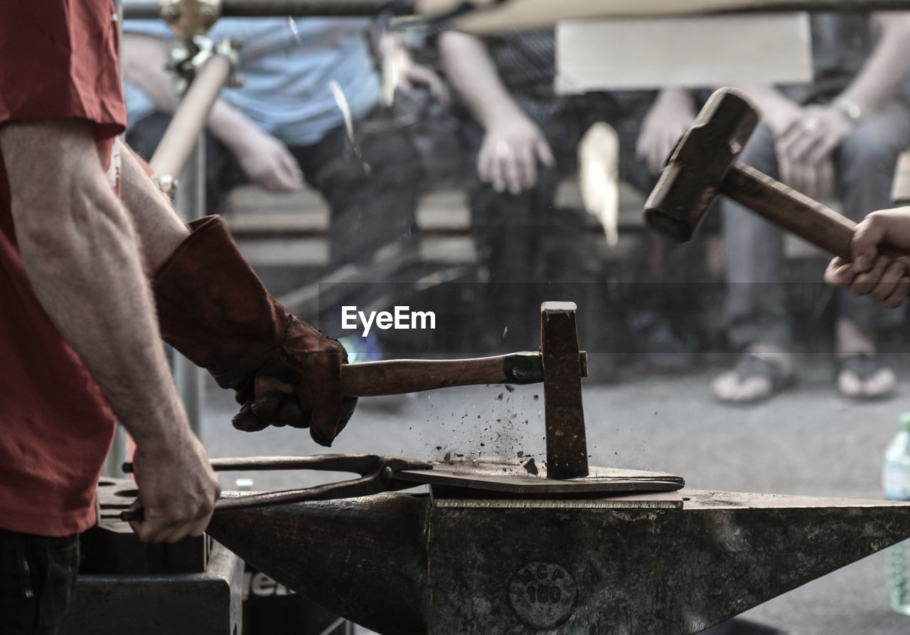 Midsection of blacksmith hammering on metal in workshop