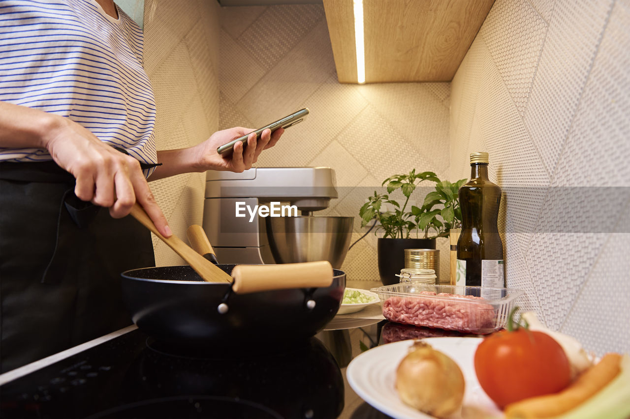 Woman cooking sauce bolognese and use smartphone