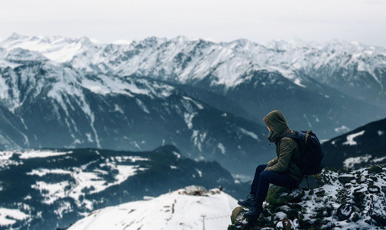 Side view of woman sitting on rock against snowcapped mountains