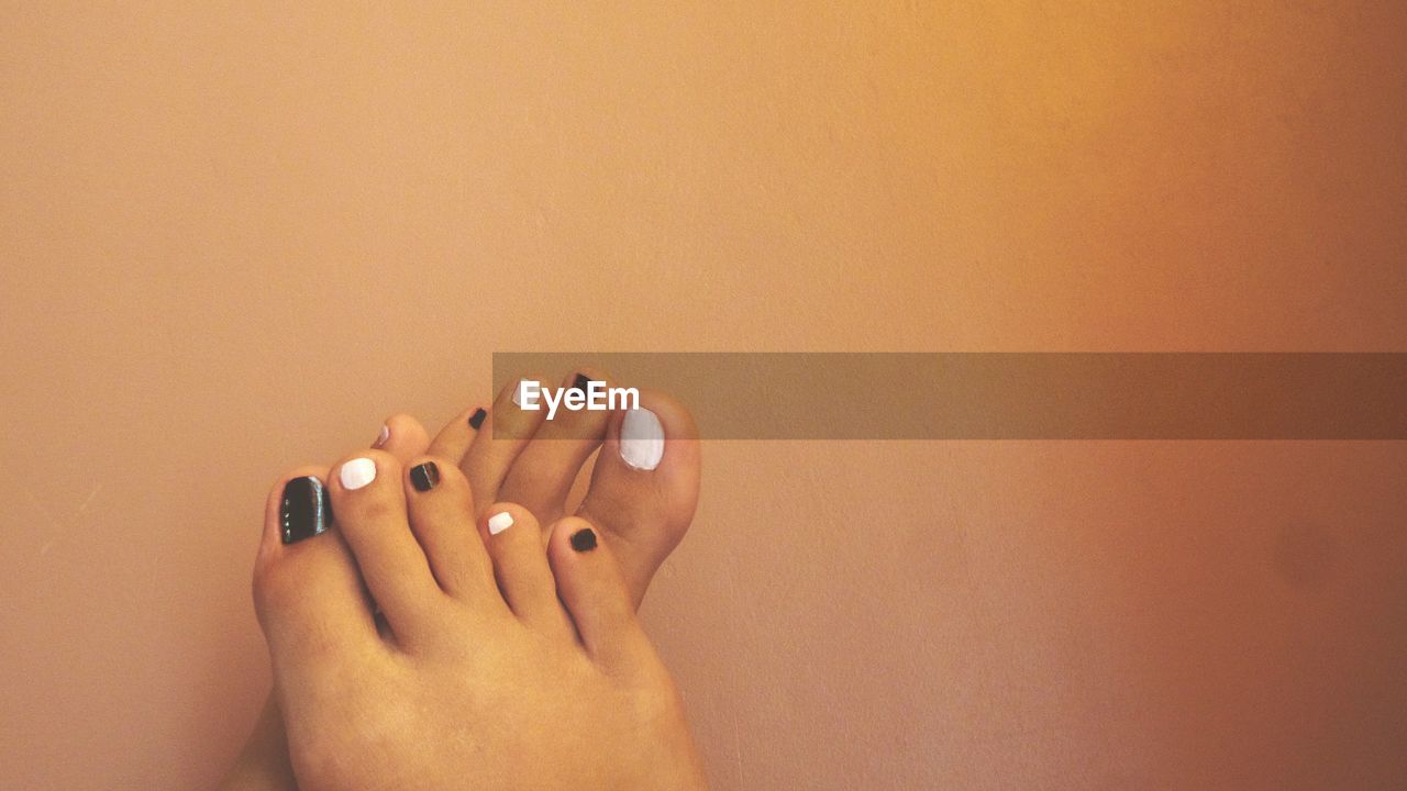 Cropped image of woman feet with nail polish against wall