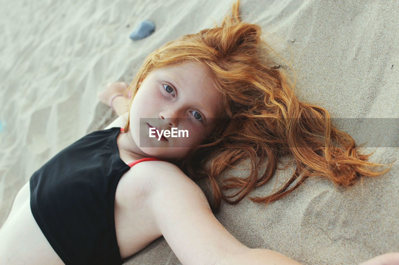 Portrait of girl with long hair lying down at sandy beach