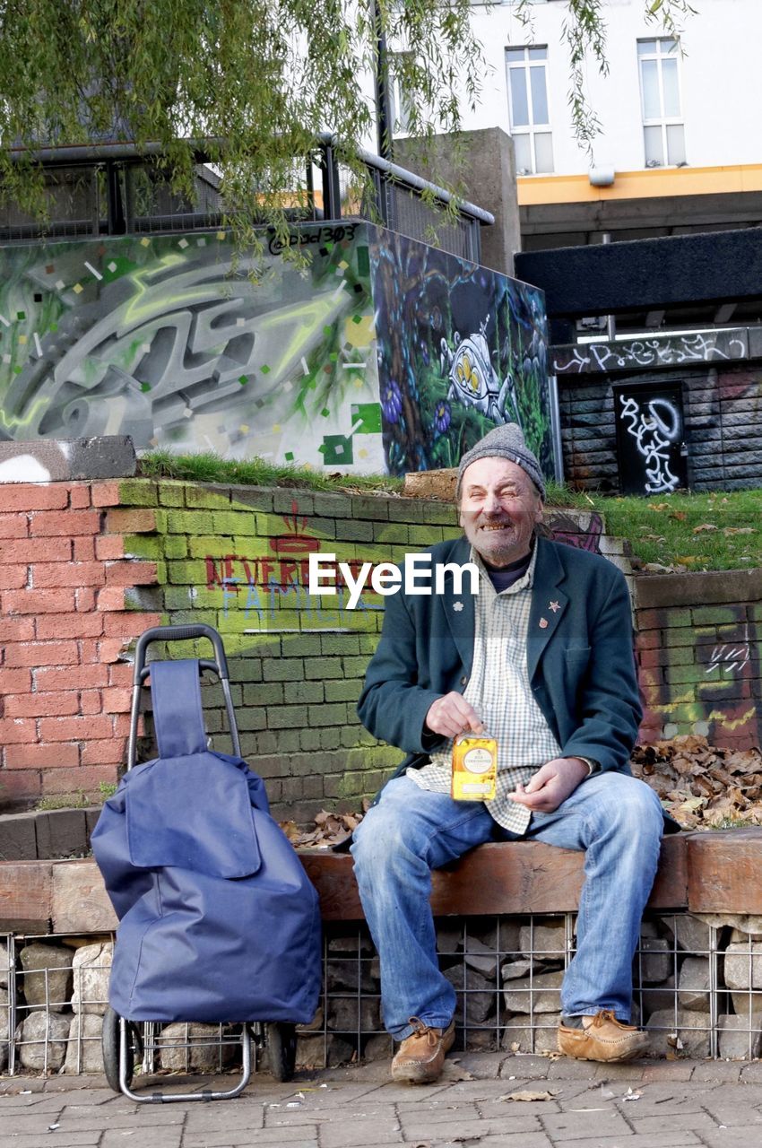 PORTRAIT OF MATURE MAN SITTING ON SIDEWALK IN CITY