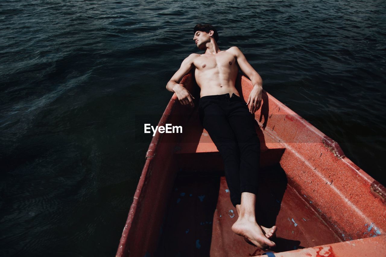 High angle view of young man sleeping in boat on lake