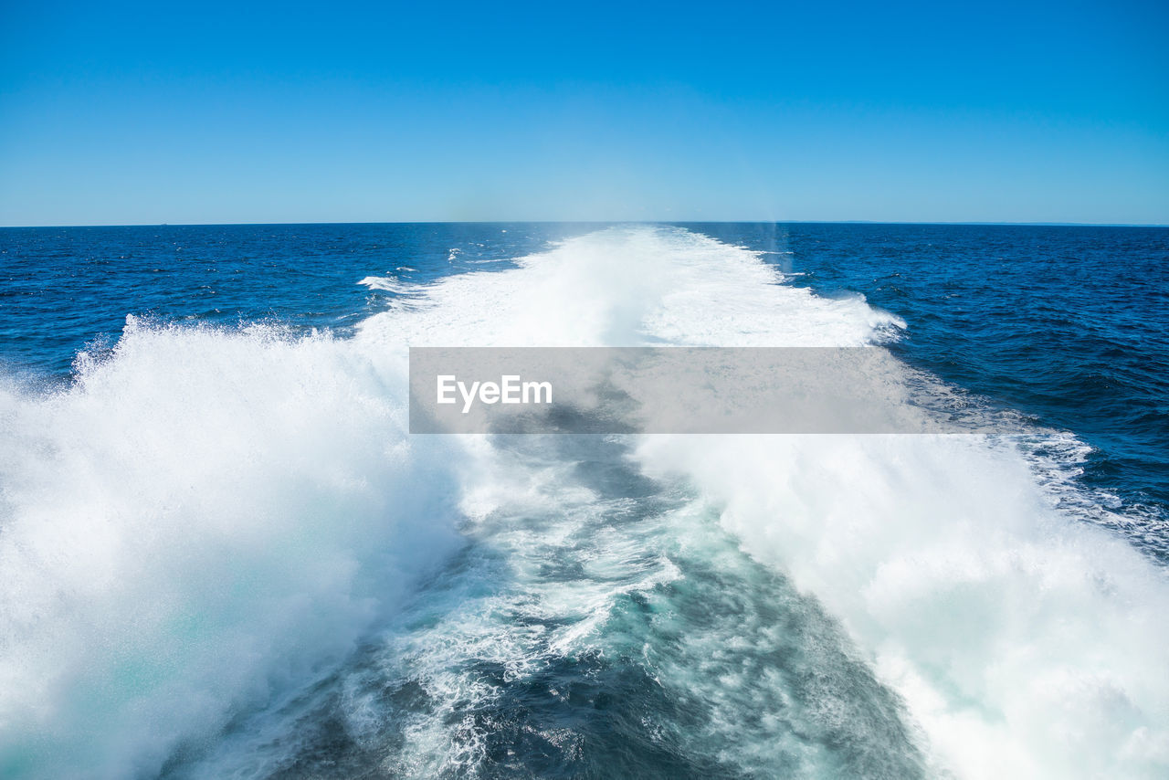 SCENIC VIEW OF SEA WAVES SPLASHING AGAINST BLUE SKY