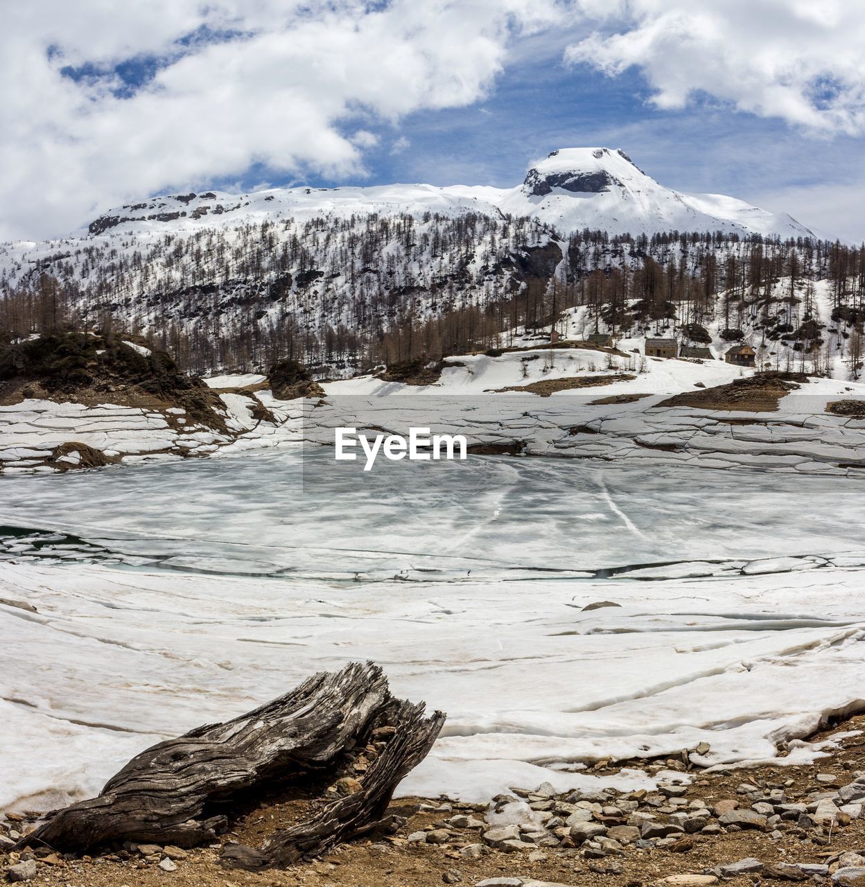 Frozen lake by snowcapped mountains against cloudy sky
