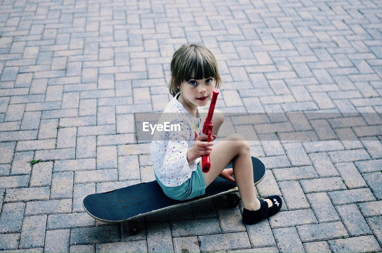 Portrait of girl holding toy gun while sitting on skateboard