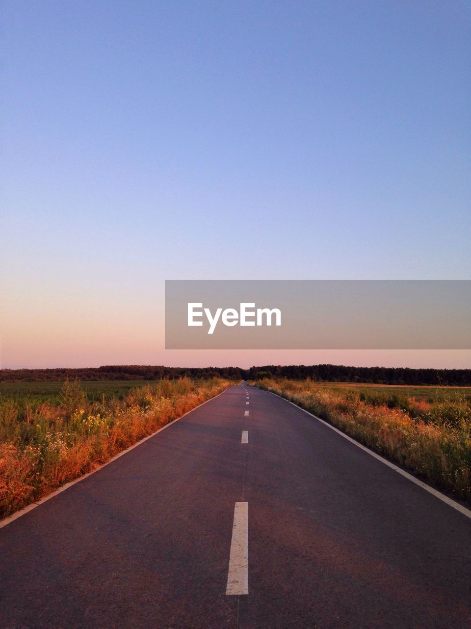 Empty road along field against clear sky 