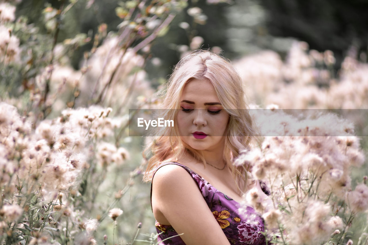 Closed-up of beautiful young woman with blond hair standing amidst flowers