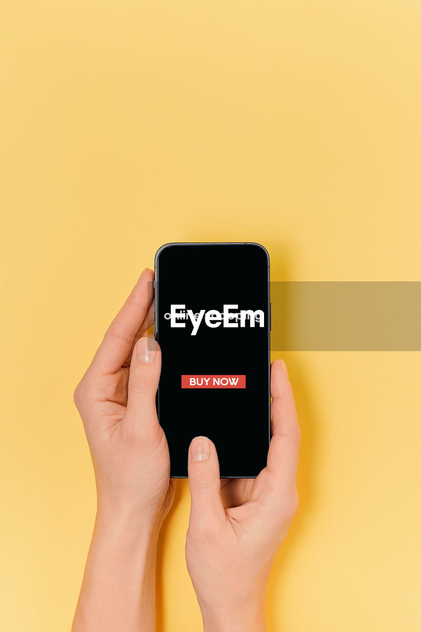 cropped hand of woman holding smart phone against yellow background