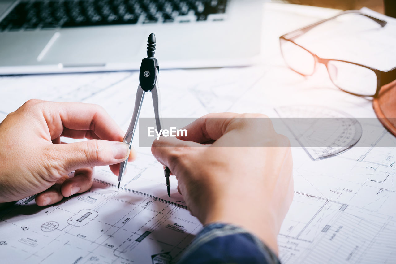 Cropped hands of person holding drawing compass on desk