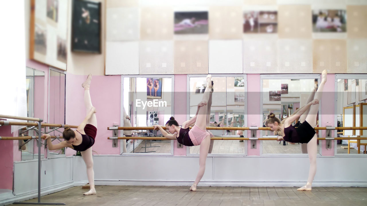 In dancing hall, young ballerinas in black leotards are stretching, standing near barre