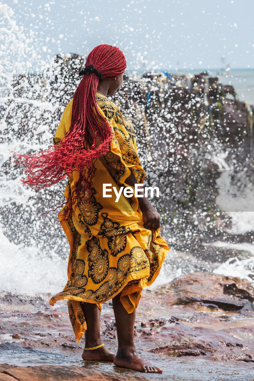 REAR VIEW OF WOMAN STANDING BY WATER SPLASHING