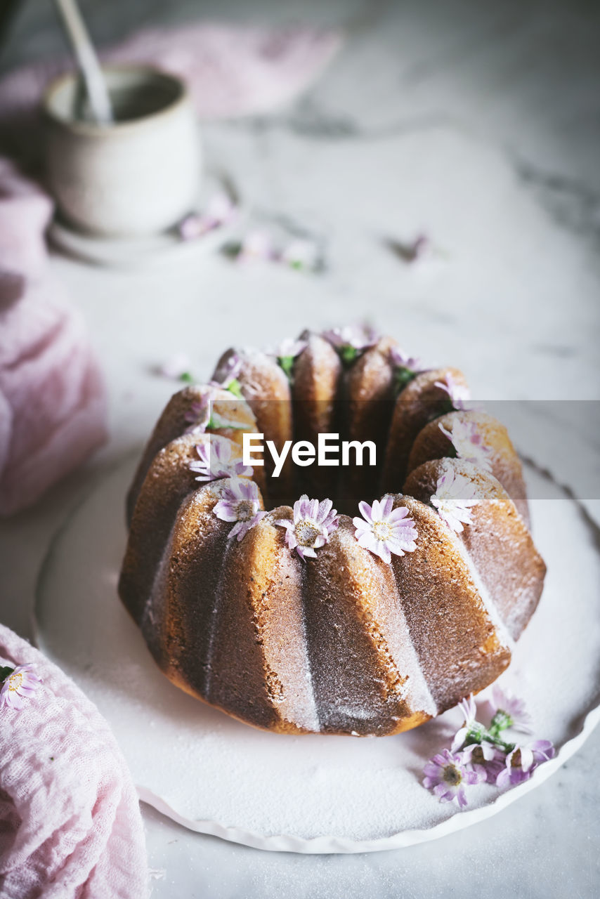 From above of tasty bundt cake decorated with fresh flowers and served on plate on table in kitchen