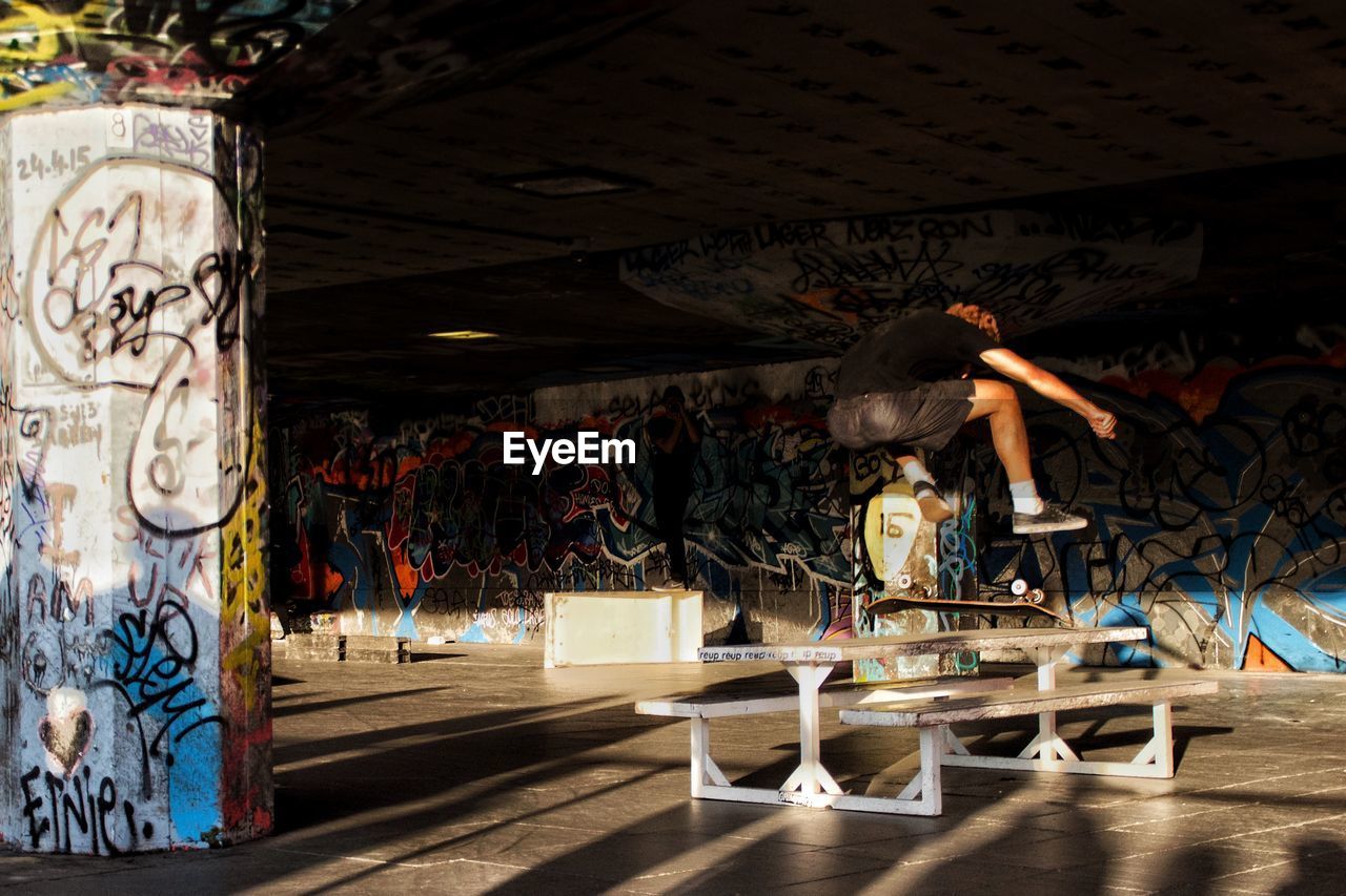 Man jumping while skateboarding against graffiti wall