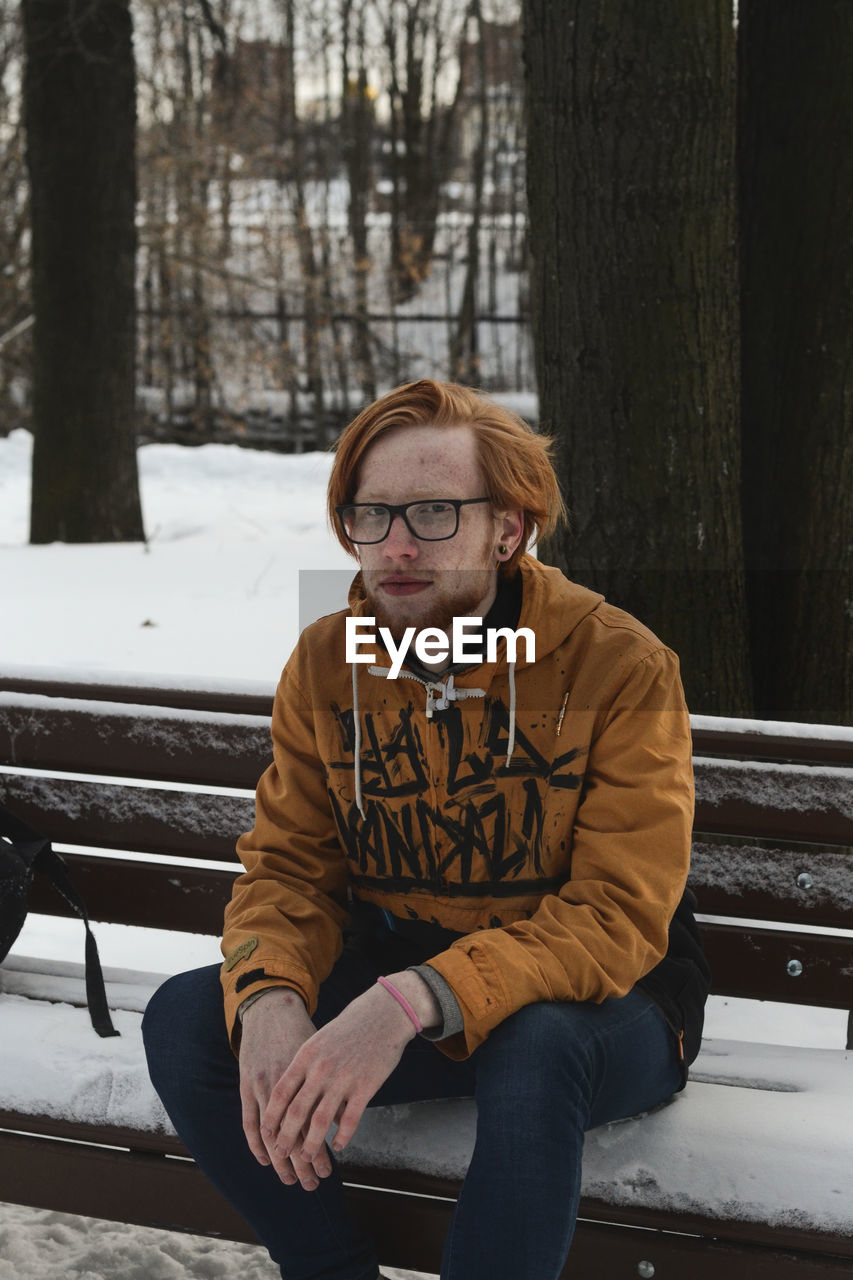 Portrait of young man sitting on bench in park during winter