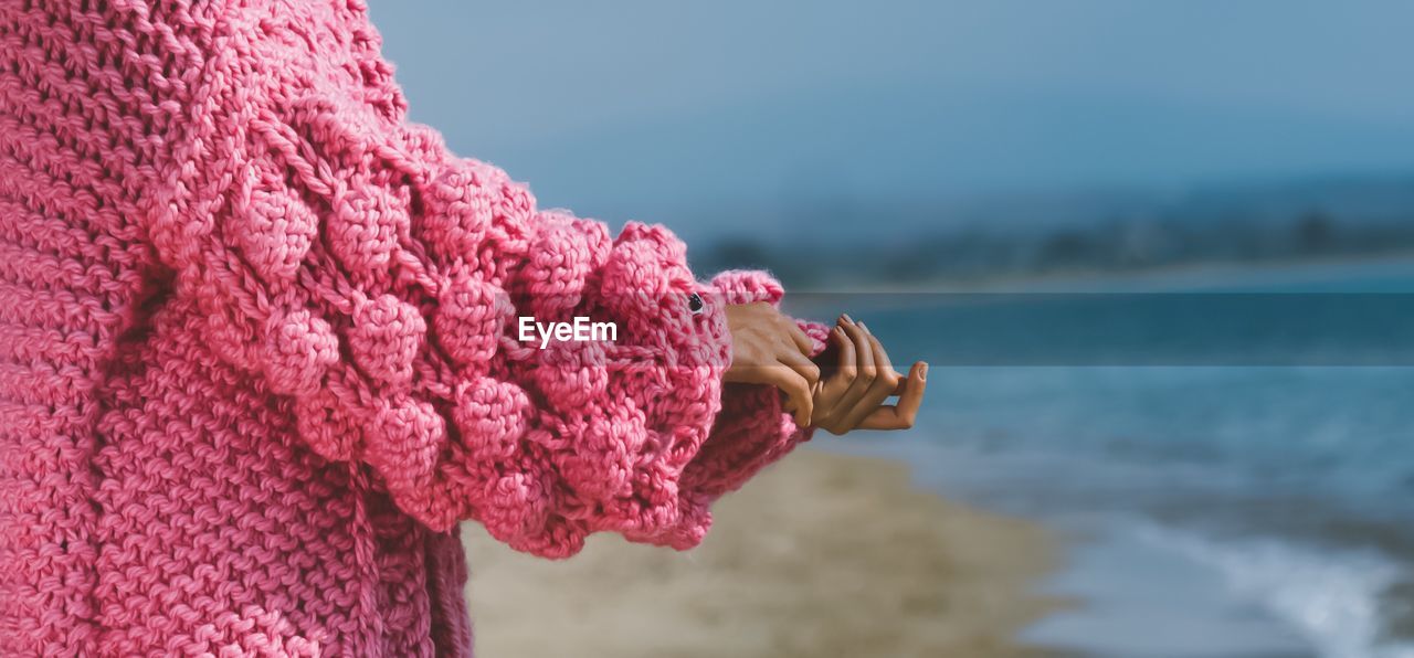 Close-up of hand on pink sweater on a beach