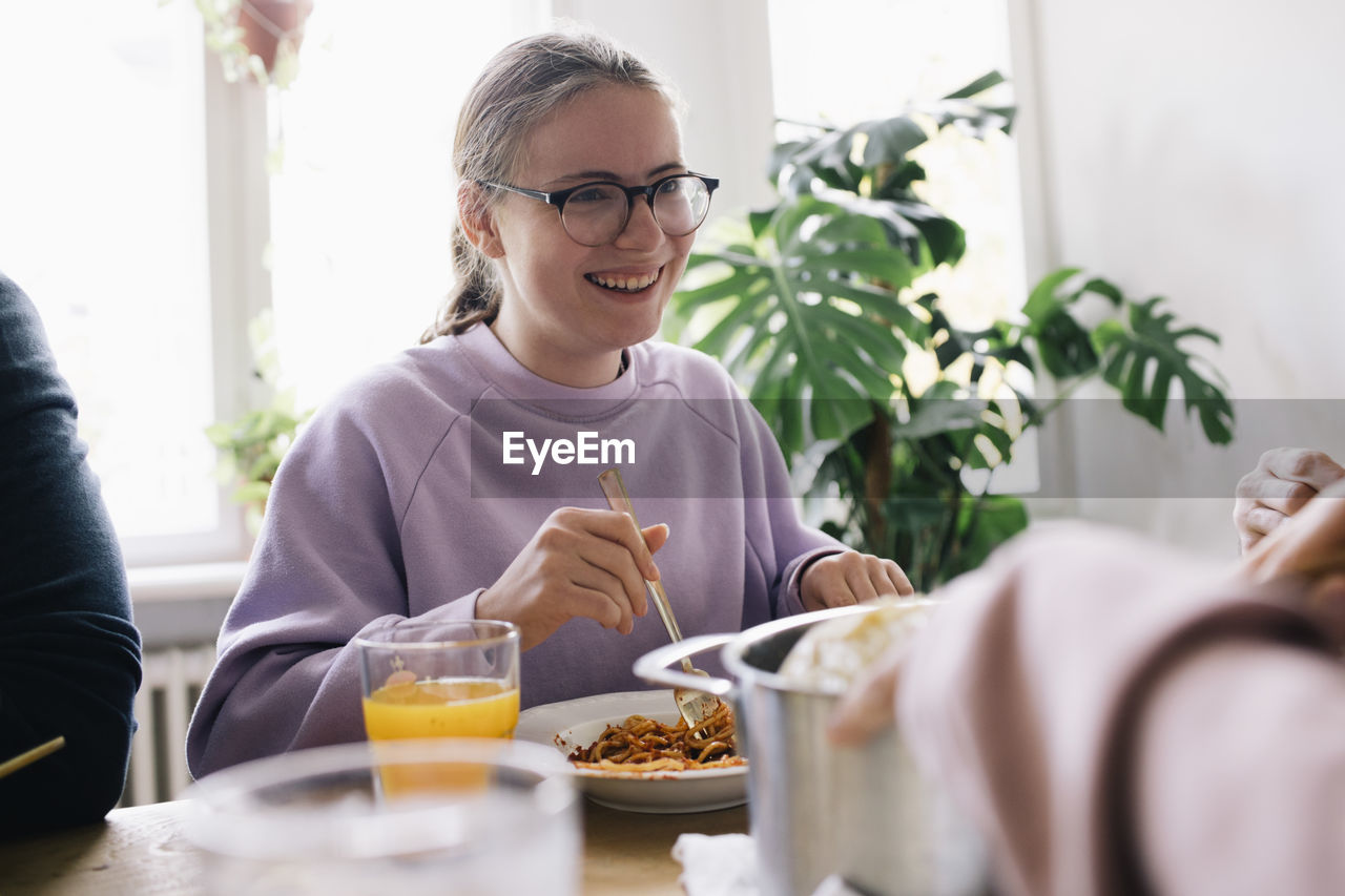 Happy woman wearing eyeglasses enjoying spaghetti at home