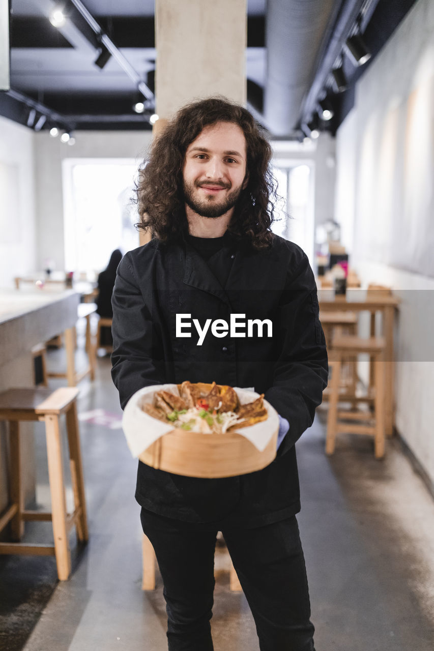 Portrait of male chef with dumplings in bowl standing at restaurant