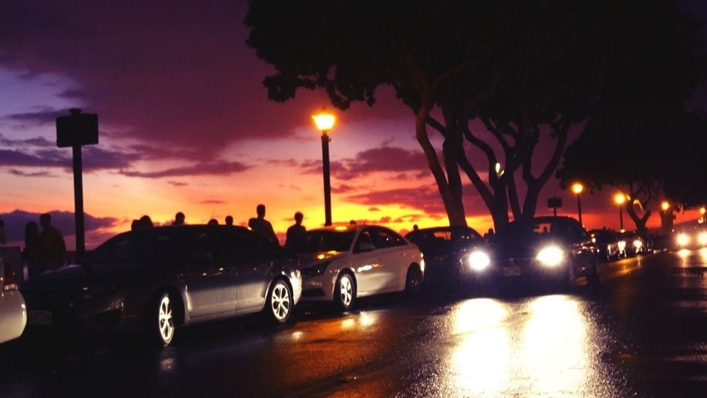 Cars on city street against sky during sunset