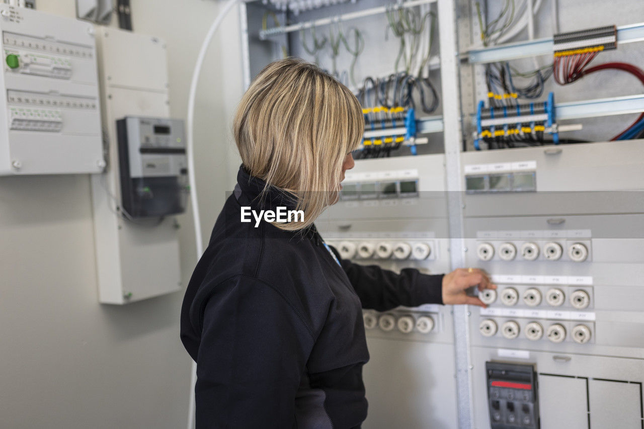 Blond female technician adjusting fuse button on meter box in control room
