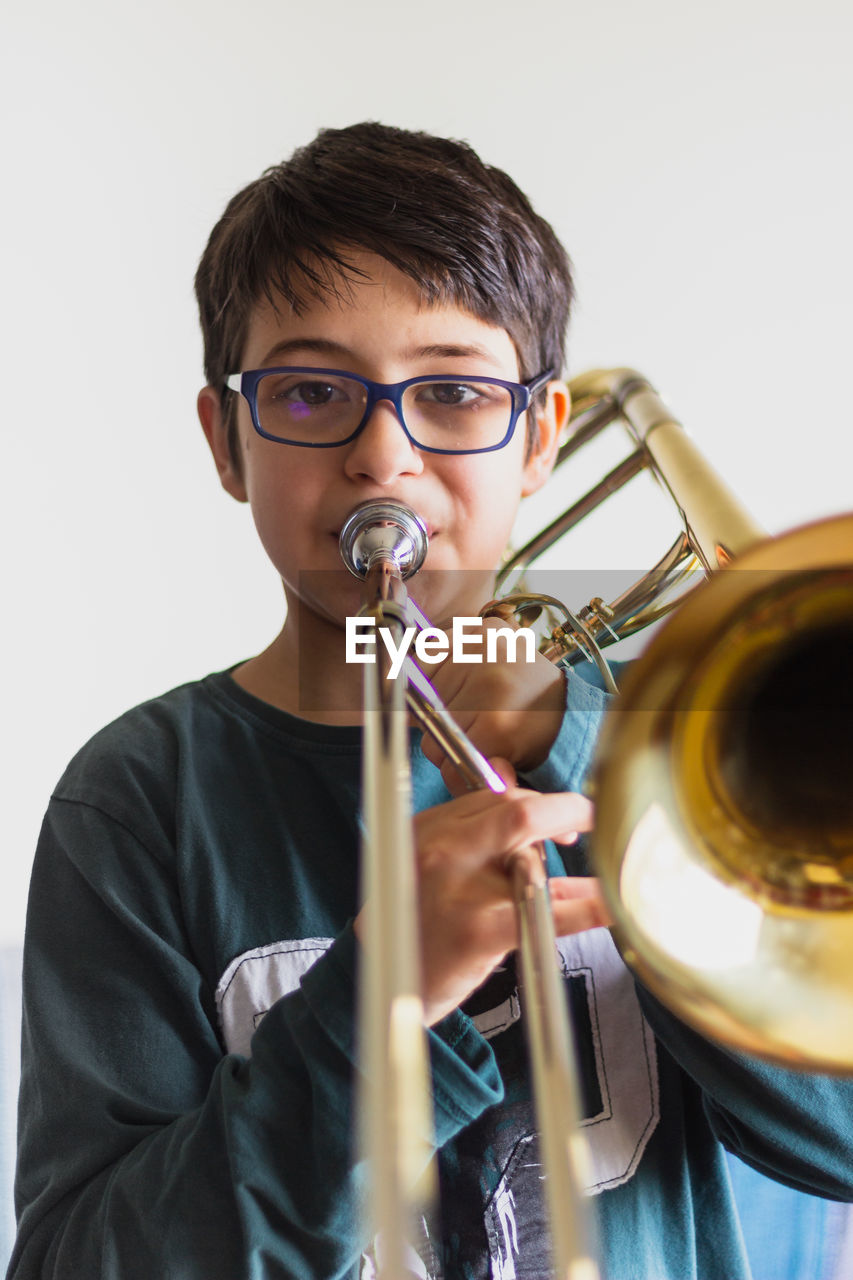 Portrait of cute boy playing trumpet against wall