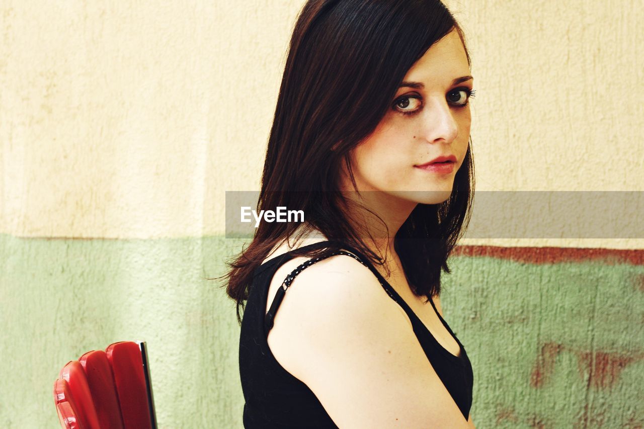 CLOSE-UP PORTRAIT OF YOUNG WOMAN STANDING AGAINST WALL