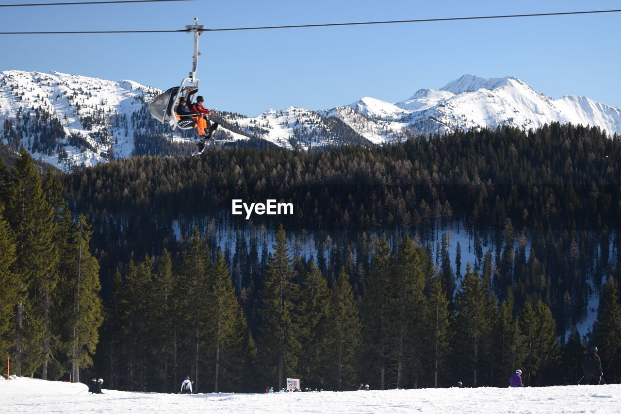 Low angle view of people sitting in ski lift against snowcapped mountains during winter