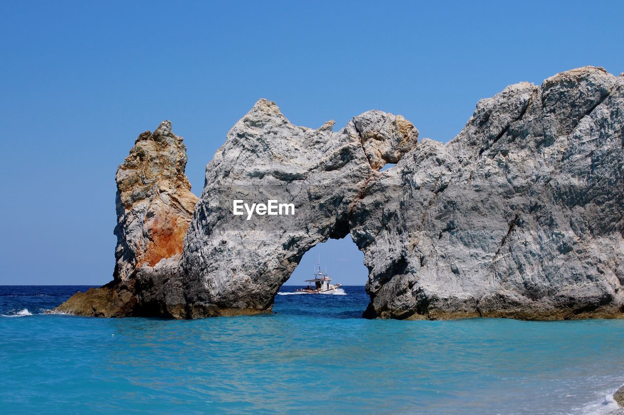 Rock formations in sea against clear blue sky