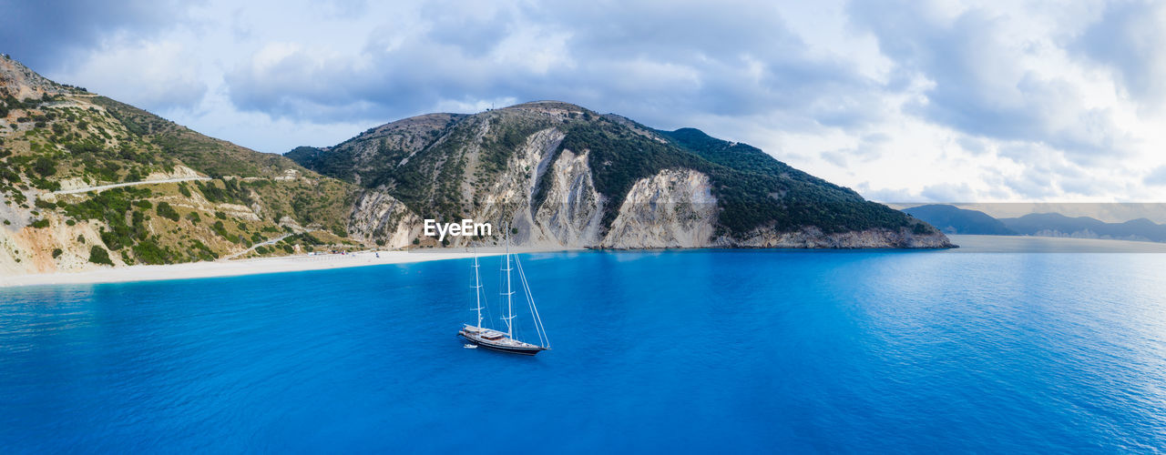 SAILBOAT IN SEA AGAINST MOUNTAIN