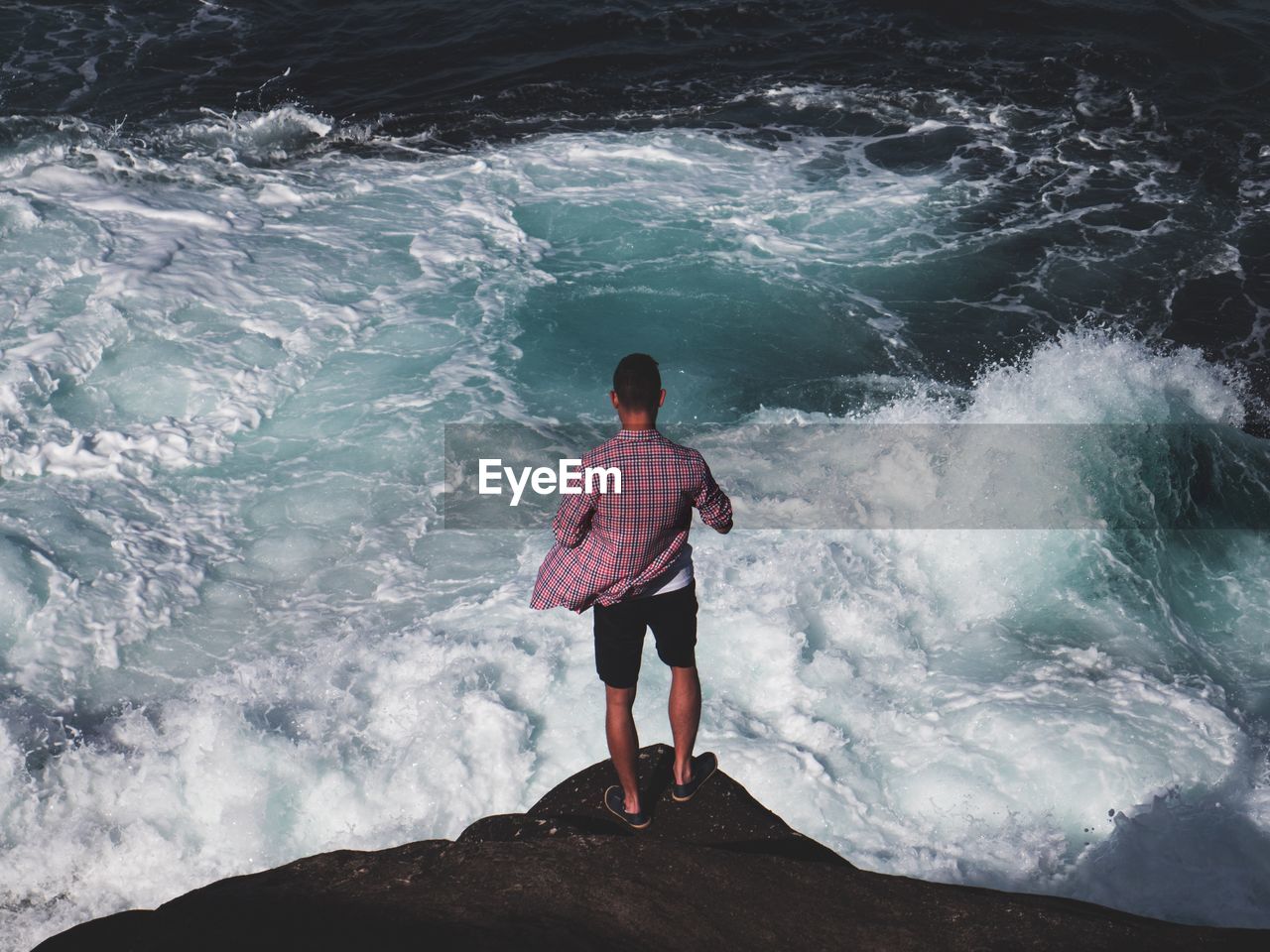 Rear view of man standing on cliff against sea