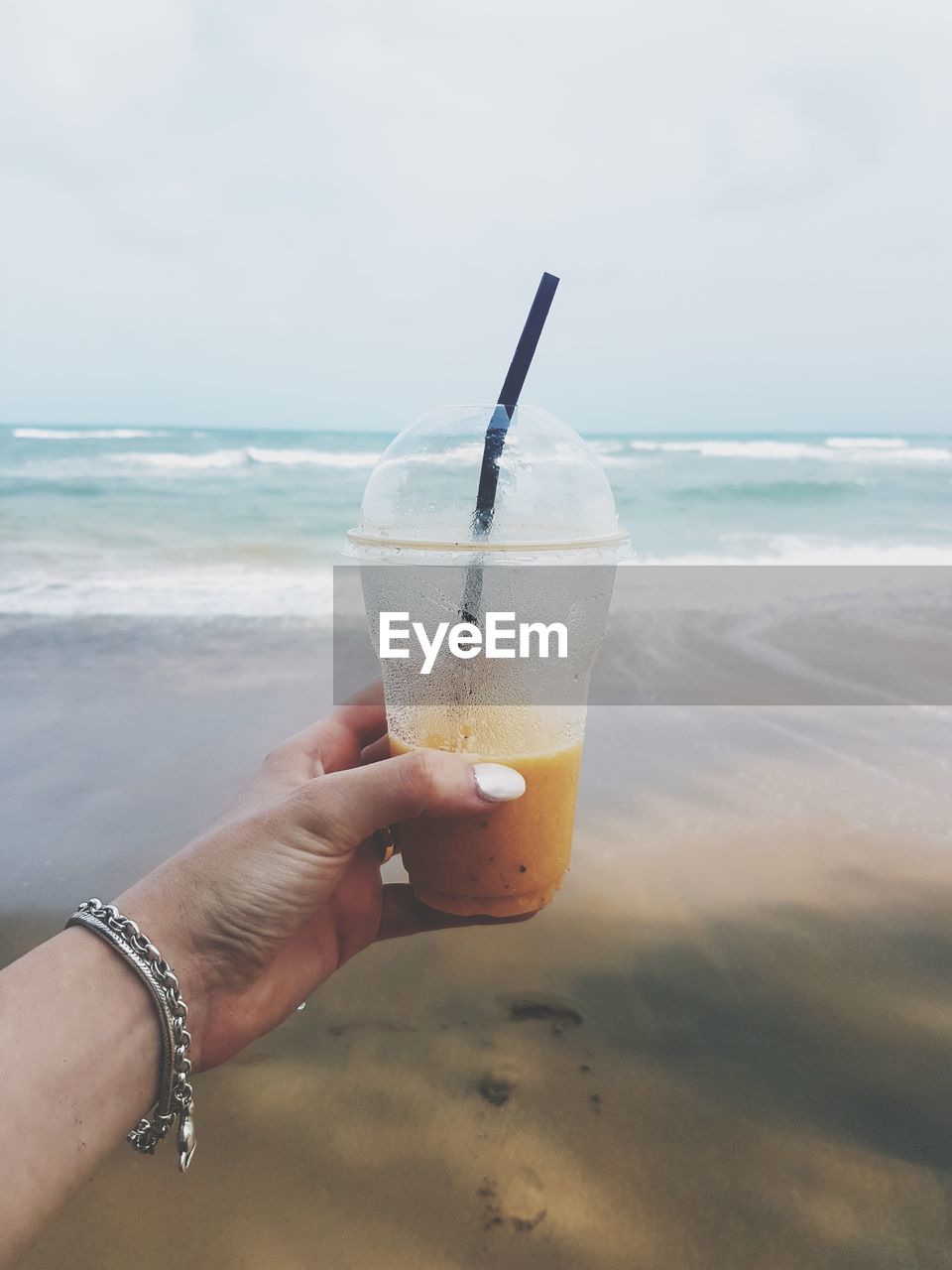 Cropped hand of woman holding disposable cup with drink at beach