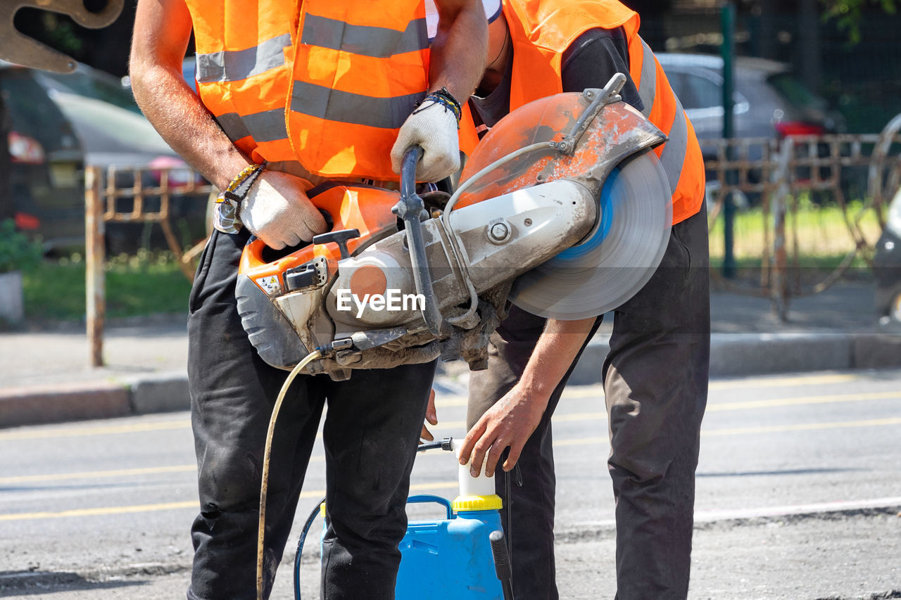 A team of workers set up the operation of a petrol disc cutter by holding .