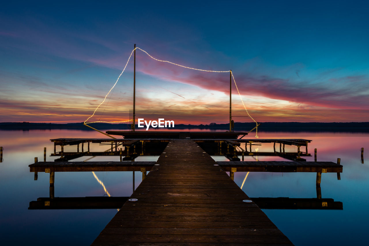 Sailboat moored at pier over lake against sky during sunset