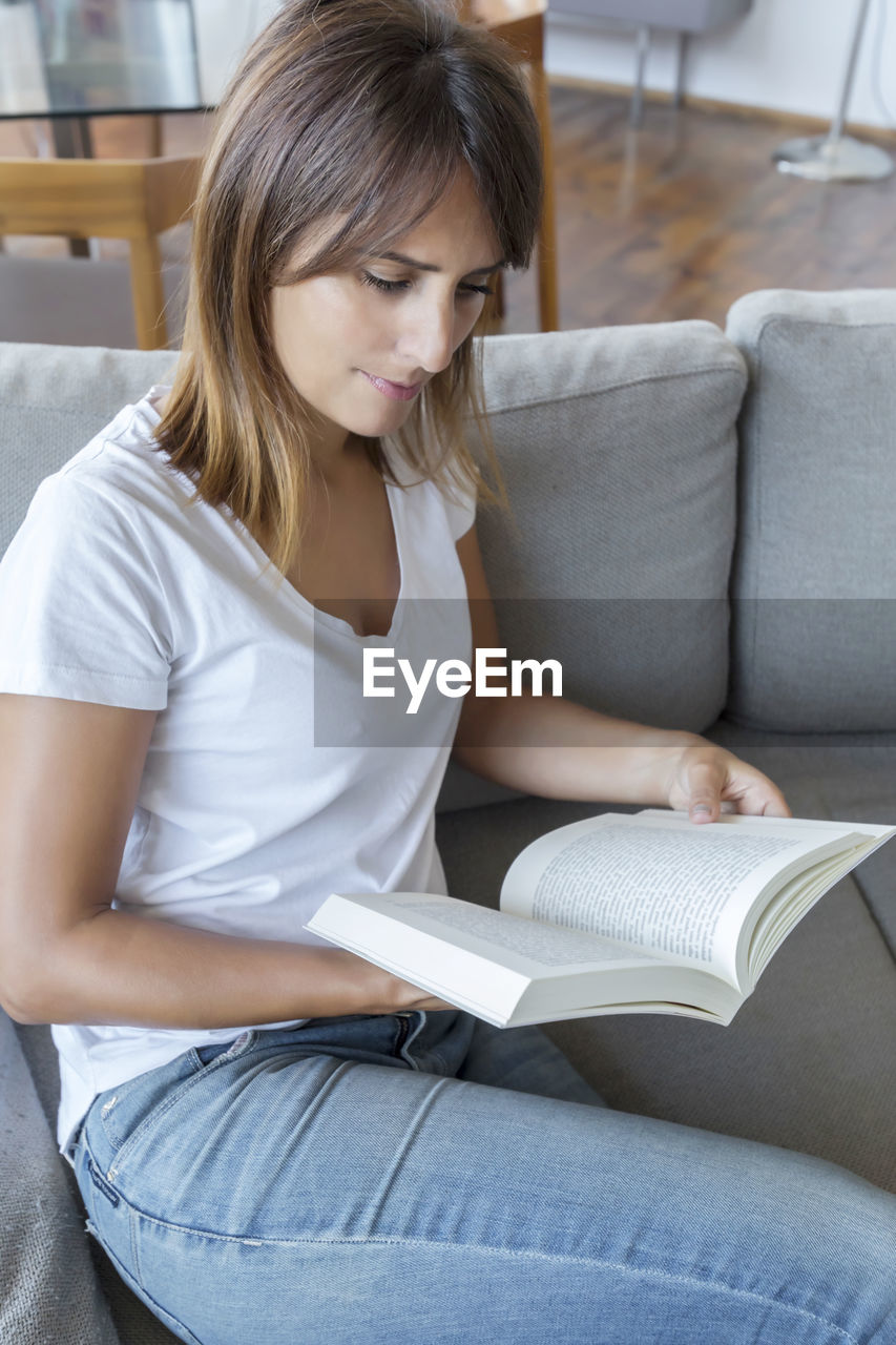 Woman reading book while sitting on sofa at home