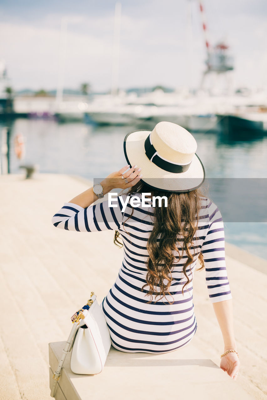 Rear view of woman in hat sitting at harbor