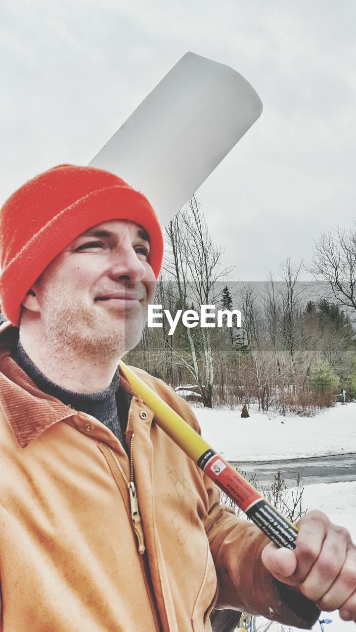 Smiling man holding shovel against sky during winter