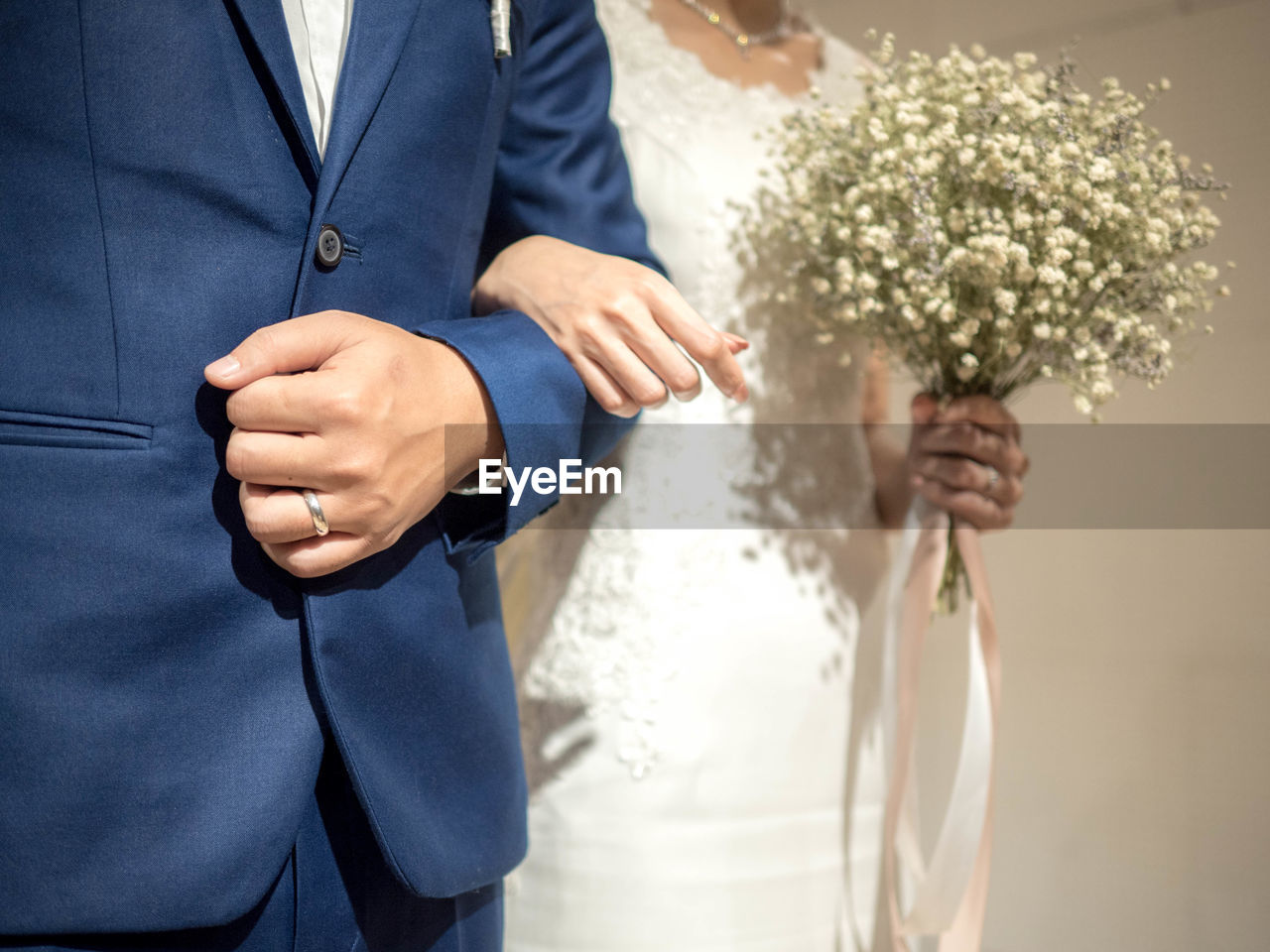 Midsection of bride and groom holding flower bouquet and hands