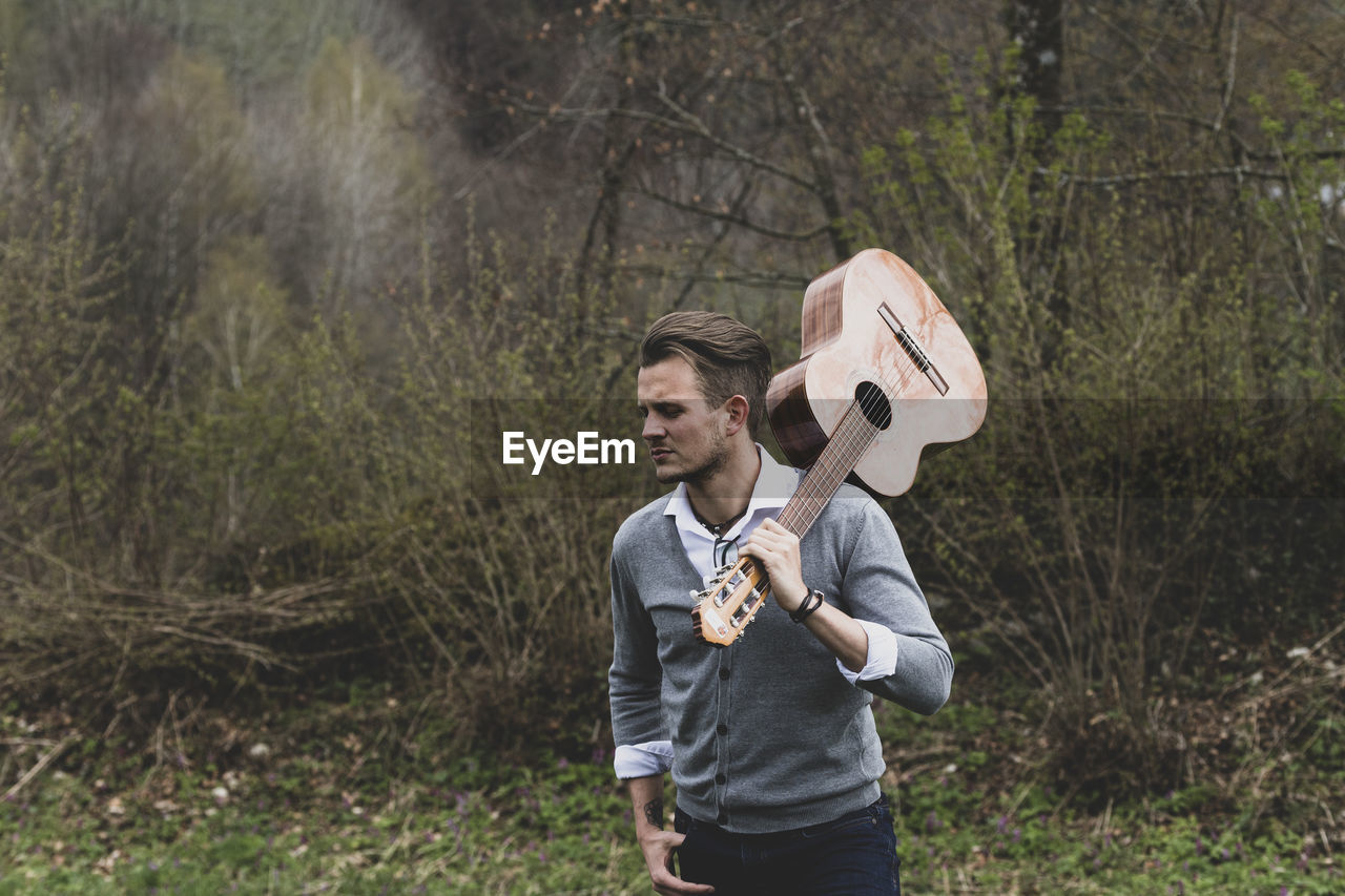 Young man with guitar standing in forest