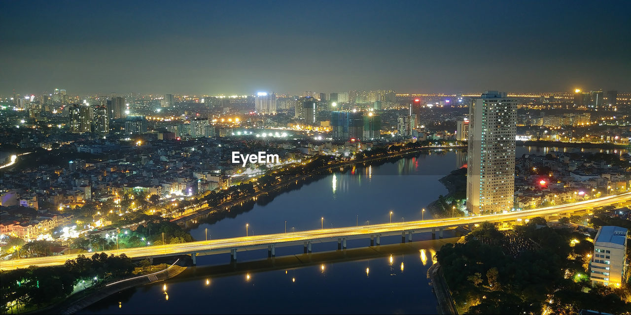 HIGH ANGLE VIEW OF ILLUMINATED BRIDGE OVER RIVER IN CITY