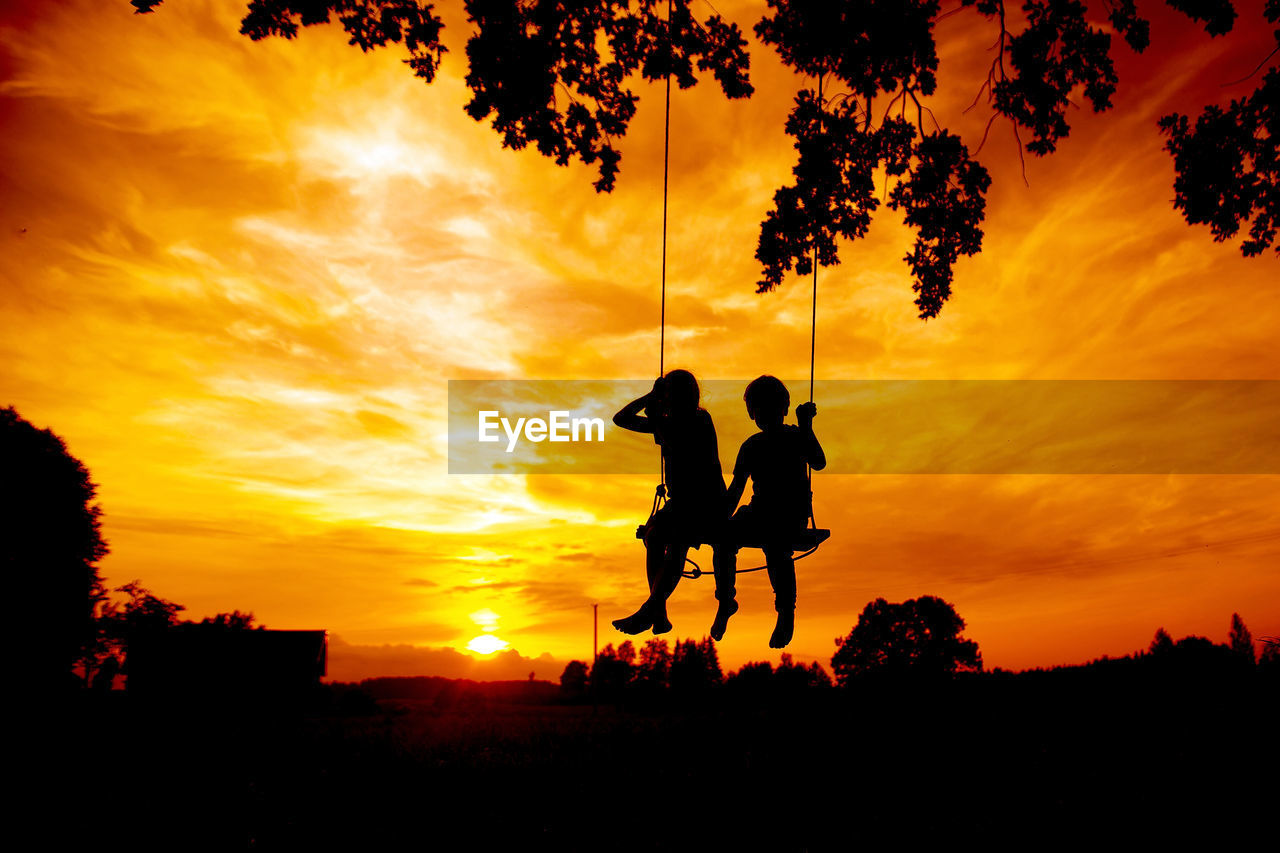 Silhouette people on swing against sky during sunset
