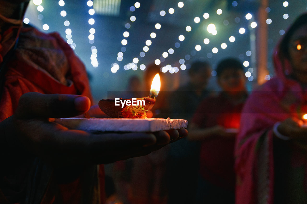 Midsection of woman holding diya while standing outdoors at night