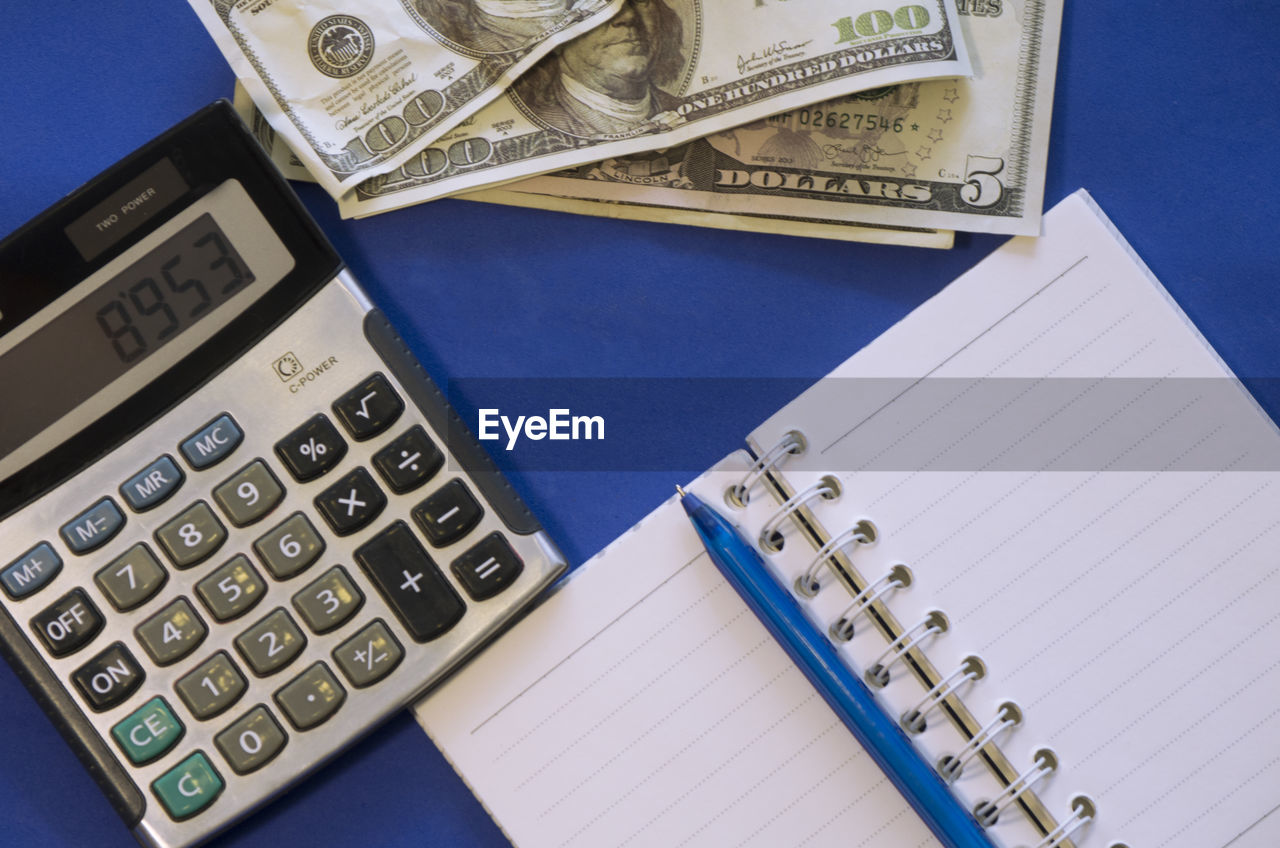 Directly above shot of paper currency with diary and calculator on blue background