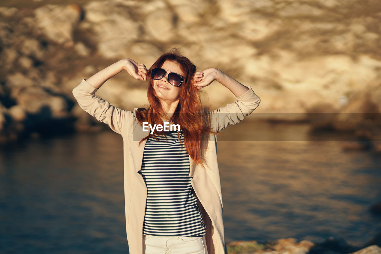 Portrait of woman wearing sunglasses standing against sea