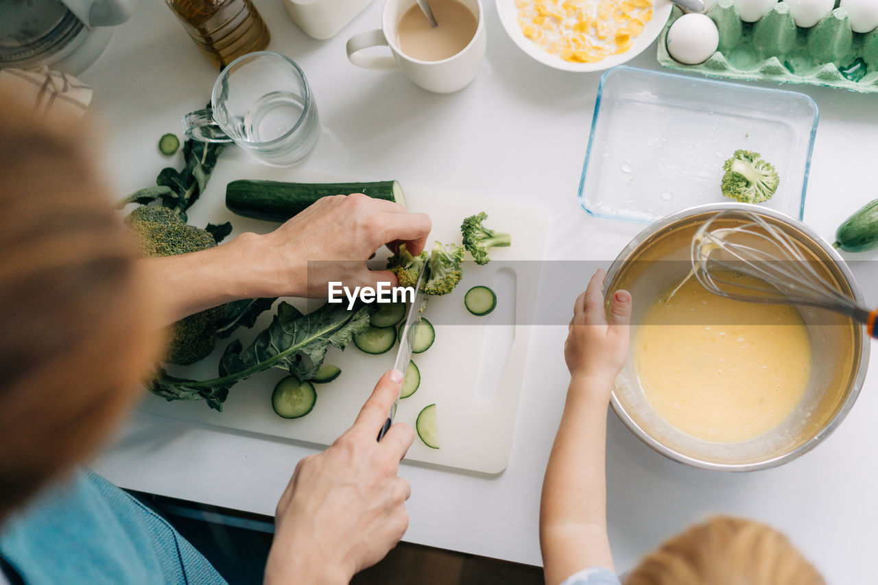 Top view of mother and daughter cooking omelet with vegetables.