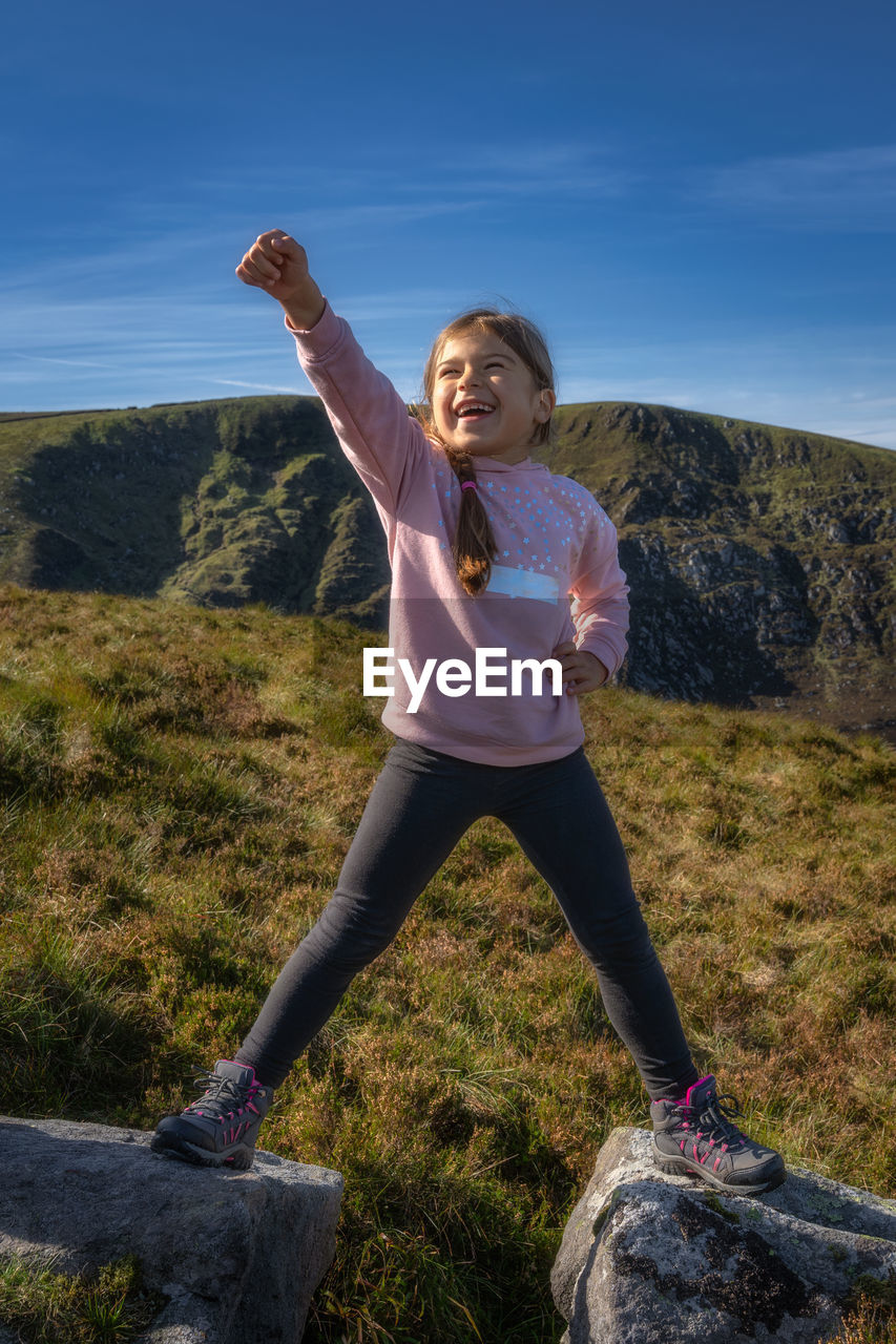 Young girl standing on two rocks with raised hand in triumph as she climbed mountain wicklow ireland